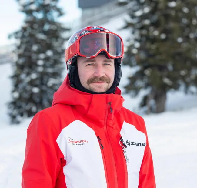 Mann in roter Ski-Ausrüstung mit Brille auf Schnee