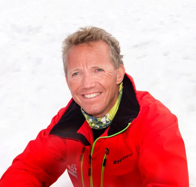 Person in roter Jacke lächelt im Schnee.
