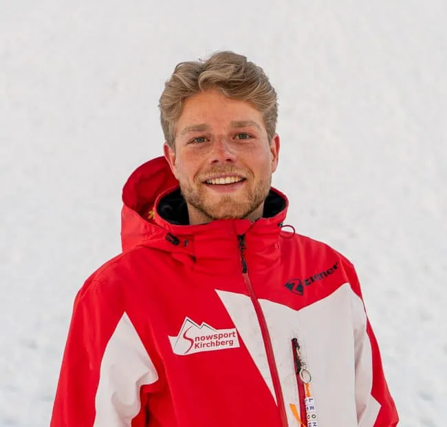 Mann mit blonden Haaren in roter Jacke, schneebedeckter Hintergrund